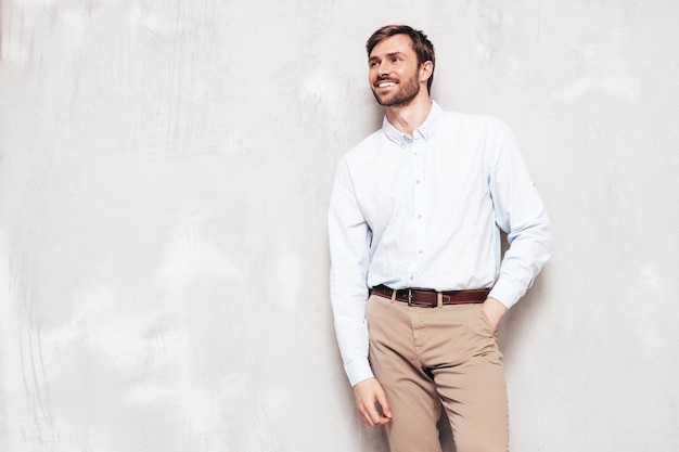 Retrato de guapo modelo sonriente Hombre elegante sexy vestido con camisa y pantalón Hombre hipster de moda posando junto a la pared gris en el estudio Aislado