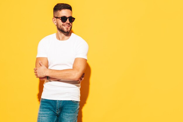 Retrato de guapo modelo sonriente Hombre elegante sexy vestido con ropa de verano Hombre hipster de moda posando junto a la pared amarilla en el estudio