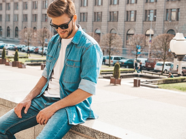 Retrato de guapo sonriente elegante hipster lumbersexual empresario modelo. Hombre vestido con ropa de chaqueta de jeans.