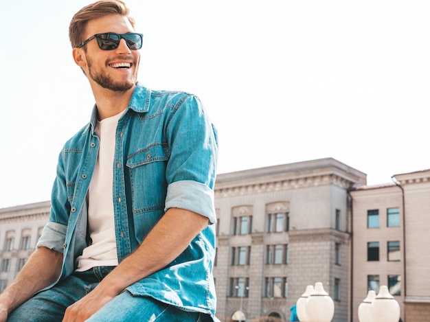 Retrato de guapo sonriente elegante hipster lumbersexual empresario modelo. Hombre vestido con ropa de chaqueta de jeans.