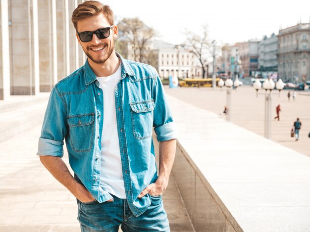 Retrato de guapo sonriente elegante hipster lumbersexual empresario modelo. Hombre vestido con ropa de chaqueta de jeans.