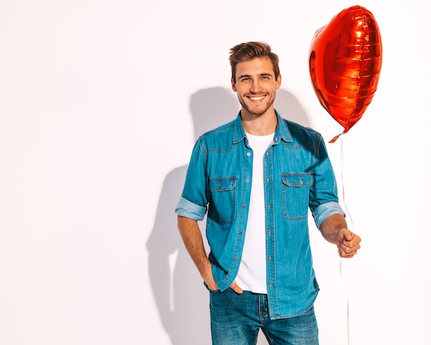 Retrato de guapo sonriente elegante hombre modelo vestido con ropa de jeans. Hombre de moda con globo en forma de corazón.