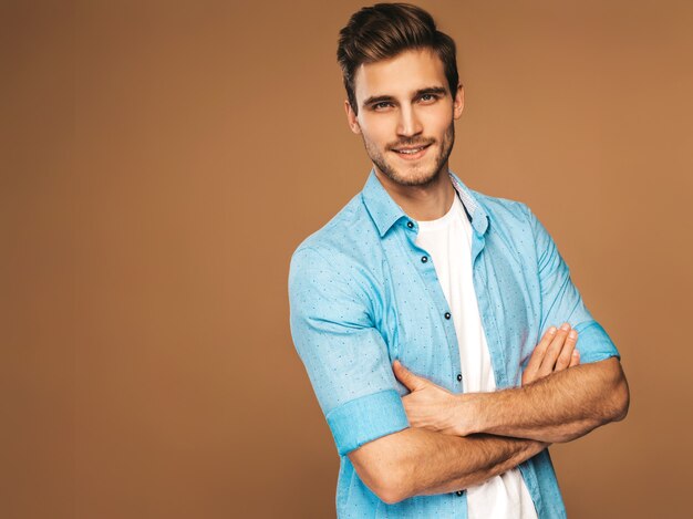 Retrato de guapo sonriente elegante joven modelo vestido con camisa azul ropa. Hombre de moda posando. Brazos cruzados