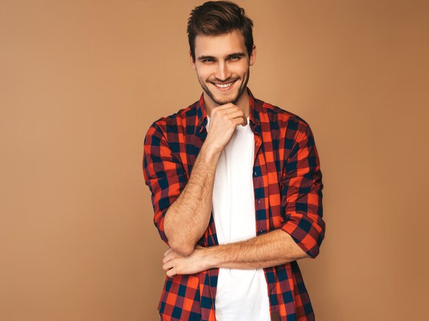 Retrato de guapo sonriente elegante joven modelo vestido con camisa a cuadros roja. Hombre de moda posando. Tocando su barbilla