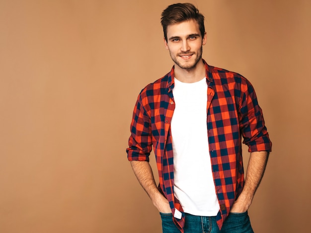 Retrato de guapo sonriente elegante joven modelo vestido con camisa a cuadros roja. Hombre de moda posando