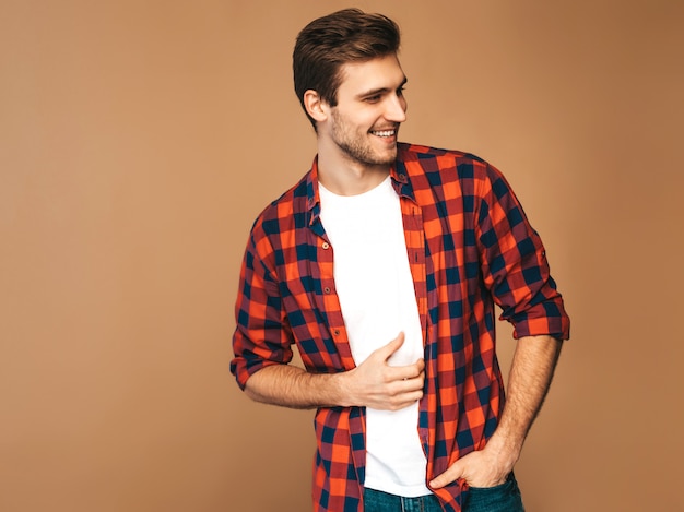 Retrato de guapo sonriente elegante joven modelo vestido con camisa a cuadros roja. Hombre de moda posando