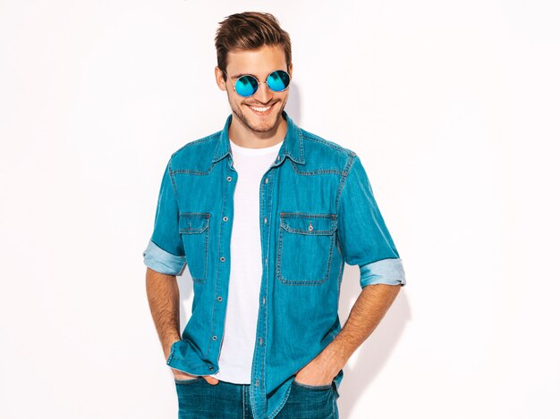 Retrato de guapo sonriente elegante joven modelo vistiendo ropa de jeans y gafas de sol. Hombre de moda