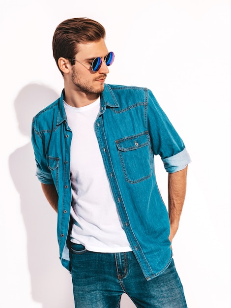 Retrato de guapo sonriente elegante joven modelo vistiendo ropa de jeans y gafas de sol. Hombre de moda