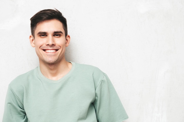 Retrato de guapo sonriente con estilo hipster lambersexual modelMan vestido con camiseta y jeans Hombre de moda aislado en el estudio Posando cerca de la pared gris Alegre y feliz