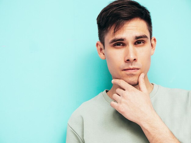 Retrato de guapo sonriente con estilo hipster lambersexual modelo Hombre vestido con camiseta y jeans Moda hombre aislado en estudio Posando cerca de la pared azul Alegre y feliz