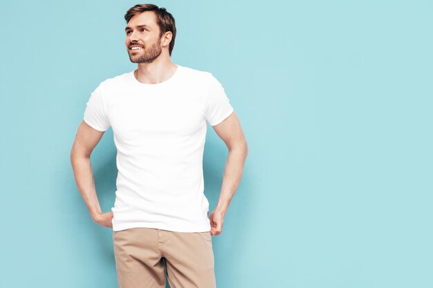 Retrato de guapo sonriente con estilo hipster lambersexual modelo Sexy hombre vestido con camiseta y pantalones Moda hombre aislado en la pared azul en el estudio