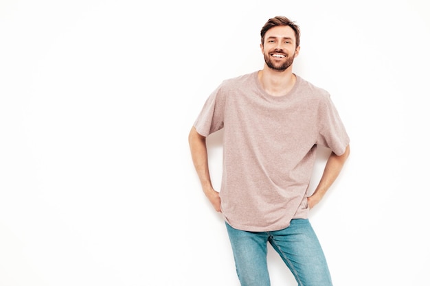 Retrato de guapo sonriente con estilo hipster lambersexual modelo Sexy hombre vestido con camiseta rosa y jeans Moda hombre aislado en la pared blanca en el estudio