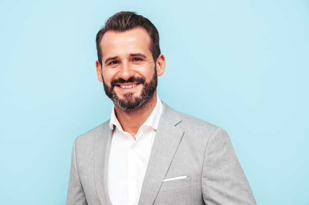 Retrato de guapo sonriente con estilo hipster lambersexual modelSexy hombre moderno vestido con traje elegante Hombre de moda posando en el estudio cerca de la pared azul