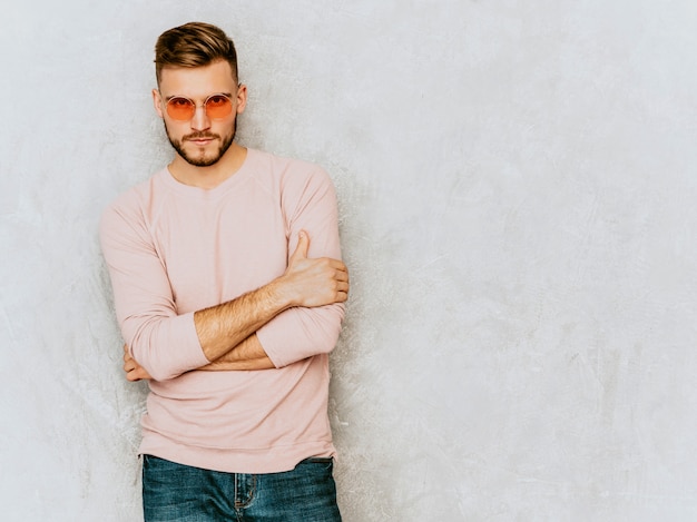 Retrato de guapo sonriente joven modelo vistiendo ropa casual verano rosa. hombre elegante moda posando en gafas de sol redondas