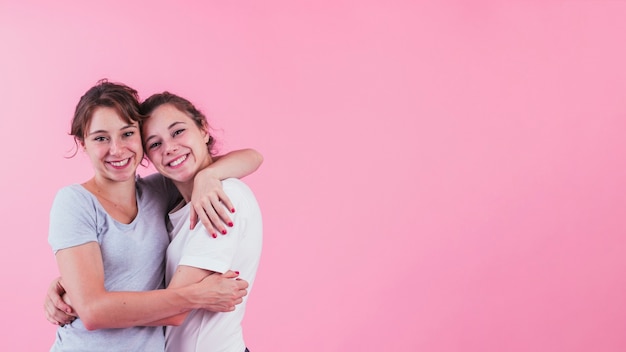 Retrato de hermana abrazándose sobre fondo rosa