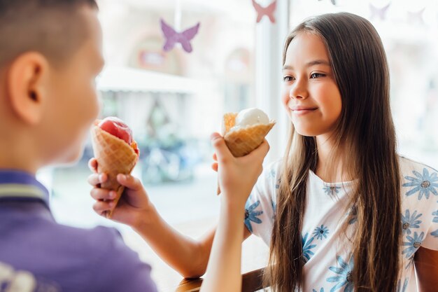 Retrato de hermana con hermano que están comiendo helado a la hora del almuerzo en casa.