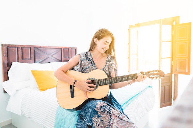 Foto gratuita retrato de hermosa adolescente sentado en la cama tocando la guitarra