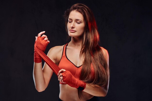 Retrato de una hermosa boxeadora morena en sujetador deportivo venda sus manos. Aislado sobre fondo oscuro con textura.