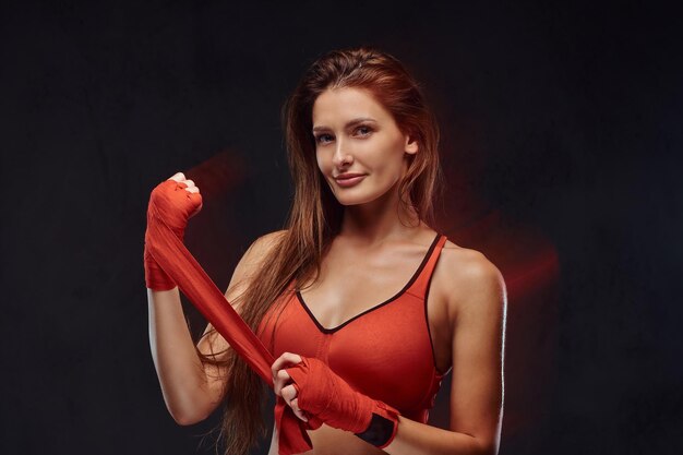 Retrato de una hermosa boxeadora morena en sujetador deportivo venda sus manos. Aislado sobre fondo oscuro con textura.