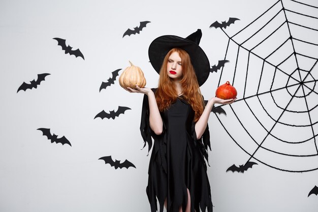 Retrato de hermosa bruja caucásica con calabaza para celebrar halloween