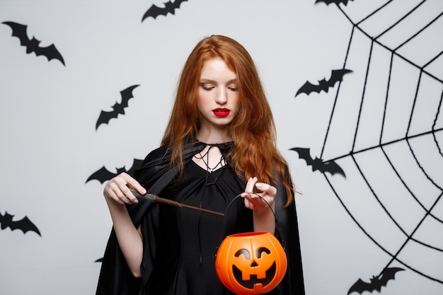 Retrato de hermosa bruja caucásica con calabaza naranja para celebrar Halloween.