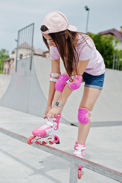 Foto gratuita retrato de una hermosa chica con camiseta de gorra y pantalones cortos poniéndose patines al aire libre junto al lago
