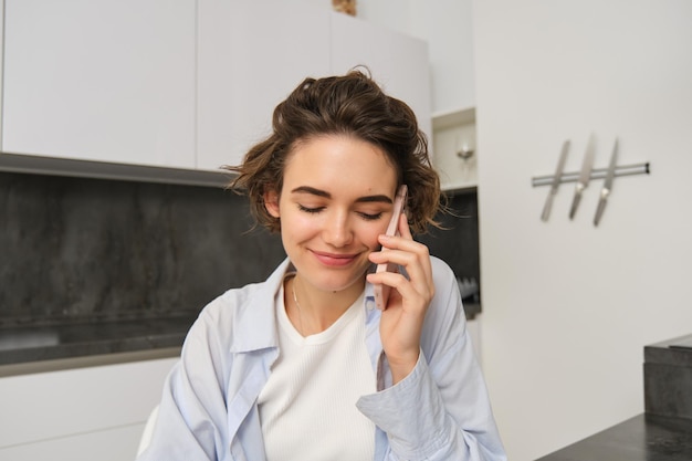 El retrato de una hermosa chica habla por teléfono móvil y tiene una conversación para responder una llamada en la cocina