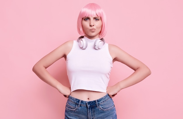 Retrato de hermosa chica hipster brillante con cabello rosado disfruta de la música en auriculares en colores