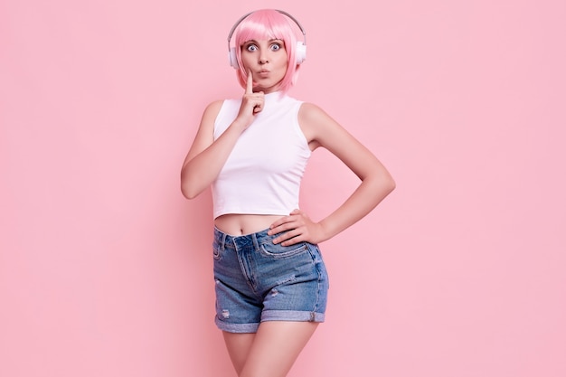 Retrato de hermosa chica hipster brillante con cabello rosado disfruta de la música en auriculares en colores