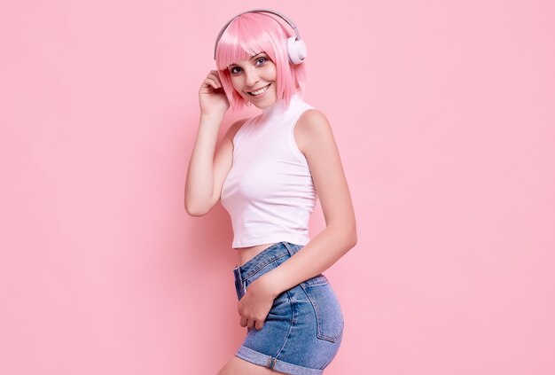 Retrato de hermosa chica hipster brillante con cabello rosado disfruta de la música en auriculares en colores