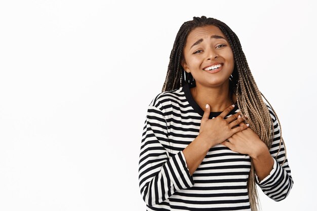 Retrato de una hermosa chica negra que mira con anhelo y ternura mostrando un gesto de latido del corazón tomados de la mano y sonriendo de pie sobre fondo blanco