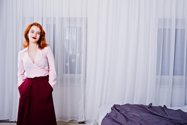 Foto gratuita retrato de una hermosa chica pelirroja con blusa y falda parada junto a la cama