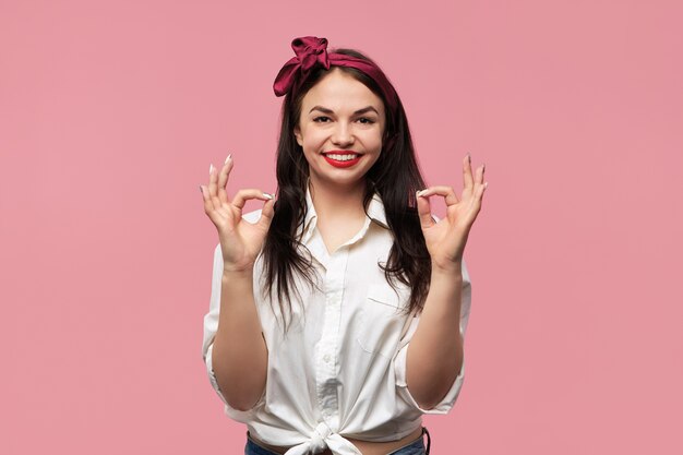 Retrato de hermosa chica pin up con camisa blanca y pañuelo rojo haciendo gesto de aprobación con ambas manos