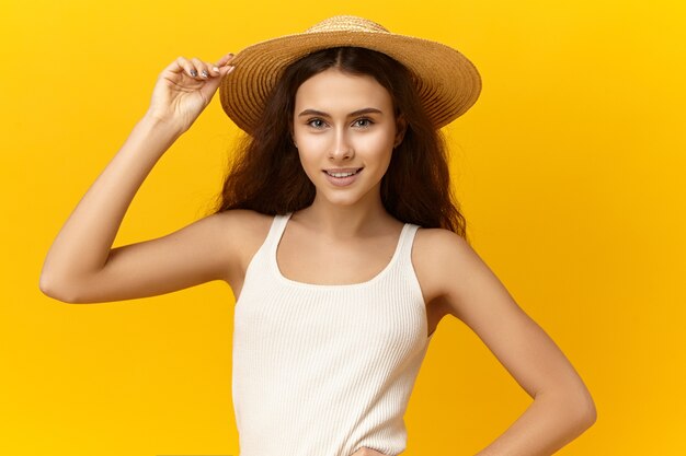 Retrato de hermosa chica romántica con estilo vistiendo camiseta blanca sin mangas y sombrero de paja