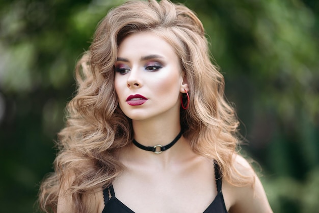 Retrato de una hermosa chica rubia Mujeres con maquillaje y hermoso cabello ondulado en una camiseta negra En un parque de la ciudad sobre un fondo verde Primer plano