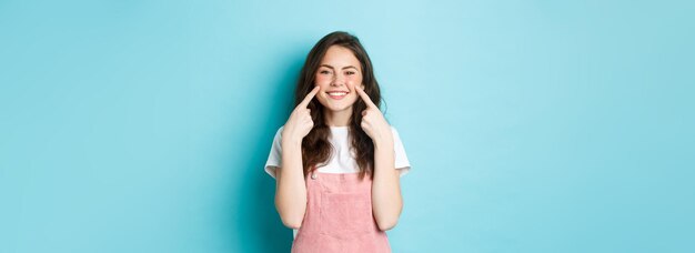 Retrato de una hermosa chica de verano metiendo las mejillas mostrando hoyuelos y dientes blancos sonrientes de pie ove