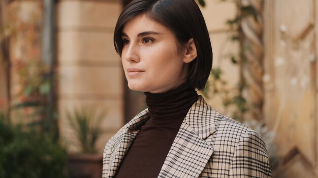 Retrato de una hermosa chica vestida con una chaqueta a cuadros y un suéter de cuello alto que parece pensativa al aire libre