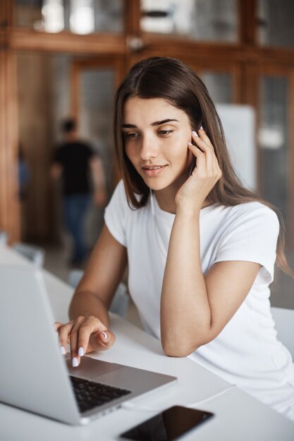 Retrato de hermosa dama usando una computadora portátil para buscar en Internet nuevos artículos y conocimientos sentados en un espacio de coworking luminoso.