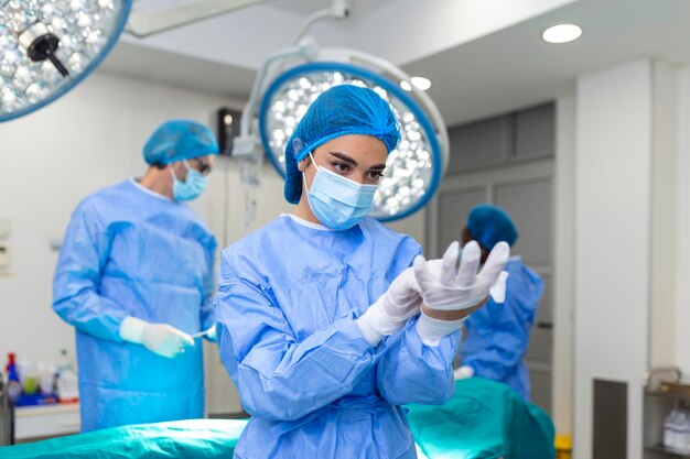 Retrato de una hermosa doctora cirujana poniéndose guantes médicos de pie en el quirófano Cirujano en el quirófano moderno