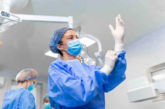 Retrato de una hermosa doctora cirujana poniéndose guantes médicos de pie en el quirófano Cirujano en el quirófano moderno