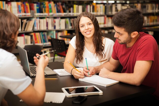 Retrato de una hermosa estudiante universitaria sonriendo mientras estudiaba con sus amigos en la biblioteca