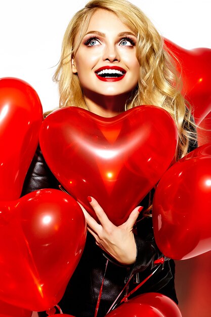 Retrato de hermosa feliz dulce sonriente mujer rubia niña sosteniendo en sus manos globos de corazón rojo en ropa casual hipster negro