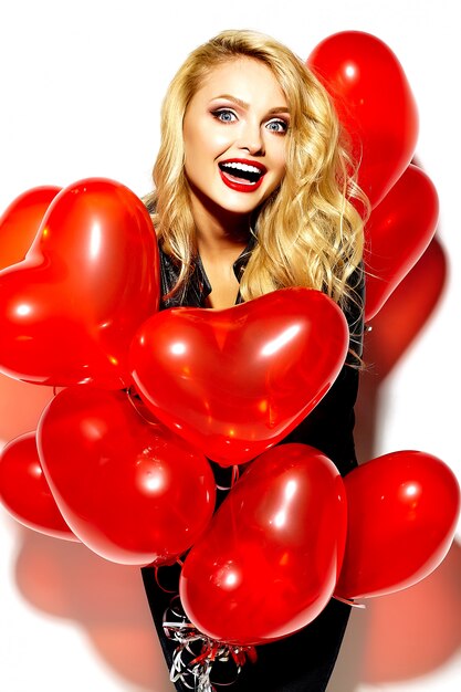 Retrato de hermosa feliz dulce sonriente mujer rubia niña sosteniendo en sus manos globos de corazón rojo en ropa casual hipster negro