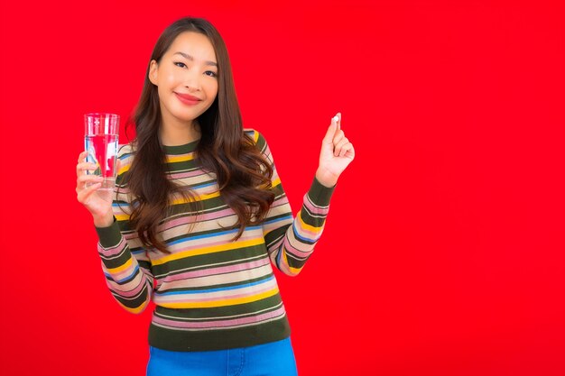 Retrato hermosa joven asiática con agua potable y píldora en la pared roja
