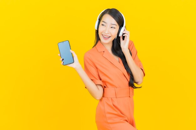 Retrato hermosa joven asiática con auriculares y teléfono móvil inteligente escuchar música en amarillo