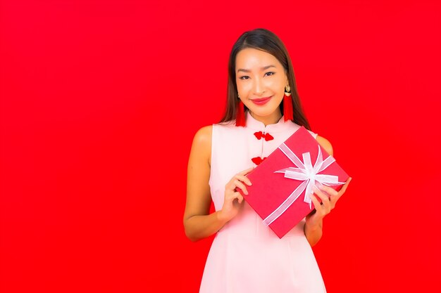 Retrato hermosa joven asiática con caja de regalo roja en pared roja aislada