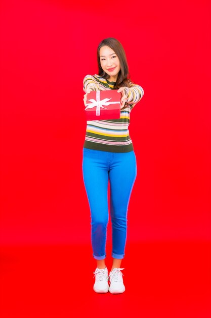 Retrato hermosa joven asiática con caja de regalo roja en la pared roja