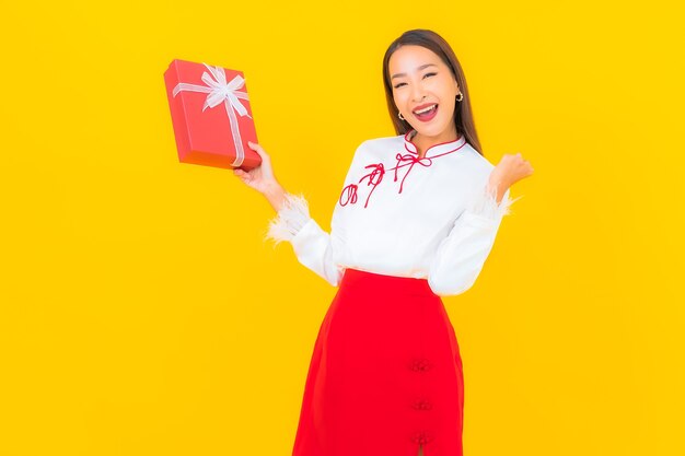 Retrato hermosa joven asiática con caja de regalo roja sobre amarillo