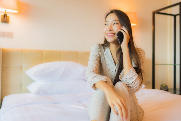 Retrato hermosa joven asiática en la cama con teléfono móvil inteligente