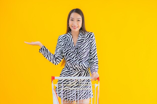 Retrato hermosa joven asiática con carrito de compras para compras en amarillo